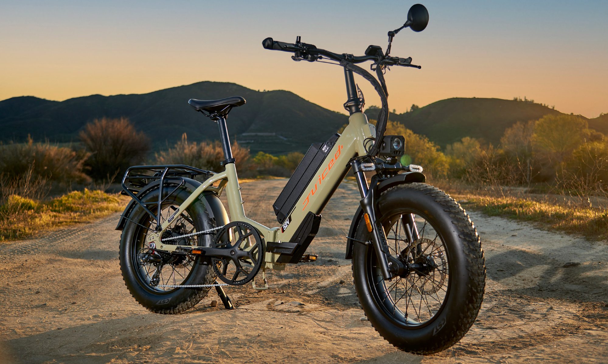 A Dessert Tan Juiced Bikes JetCurrent Pro e-bike parked on a dirt road with low vegetation hills in the background.