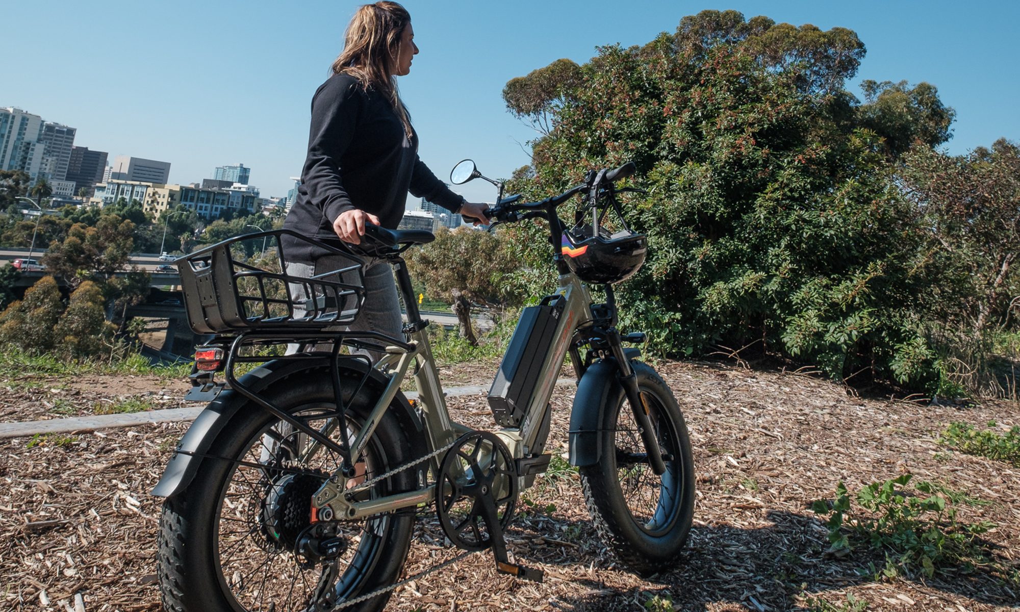 A rider standing by a Dessert Tan Juiced Bikes JetCurrent Pro e-bike on a park path.