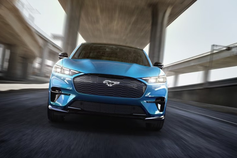 Blue 2024 Ford Mustand Mach-E GT performance upgrade driving directly at the viewer under a highway overpass.