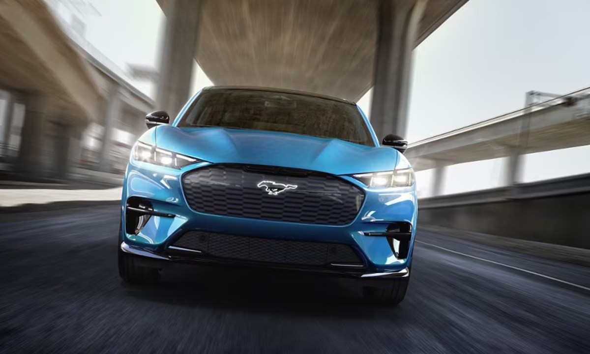 Blue 2024 Ford Mustand Mach-E GT performance upgrade driving directly at the viewer under a highway overpass.