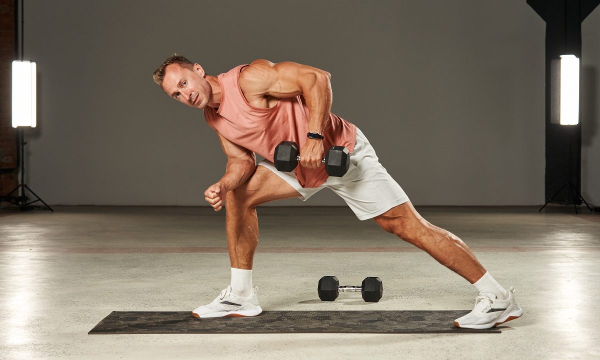One-arm dumbbell row in a bent-over position with emphasis on the leg by an athlete in shorts and a T-shirt