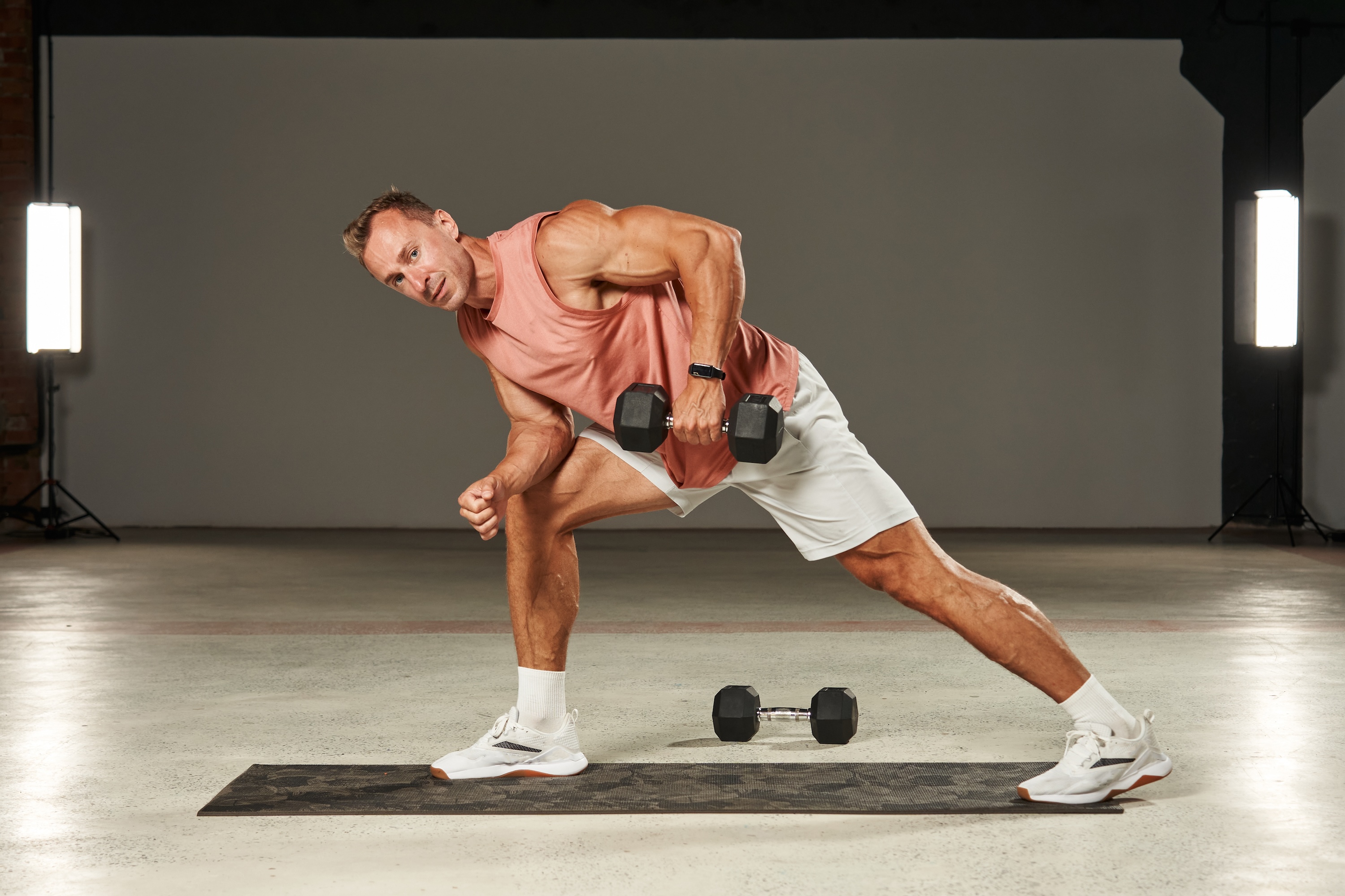 one-arm dumbbell row in a bent-over position with emphasis on the leg by a handsome Caucasian athlete in shorts and a T-shirt. fitness . aerobics. exercises on the mat. physical health. High quality photo