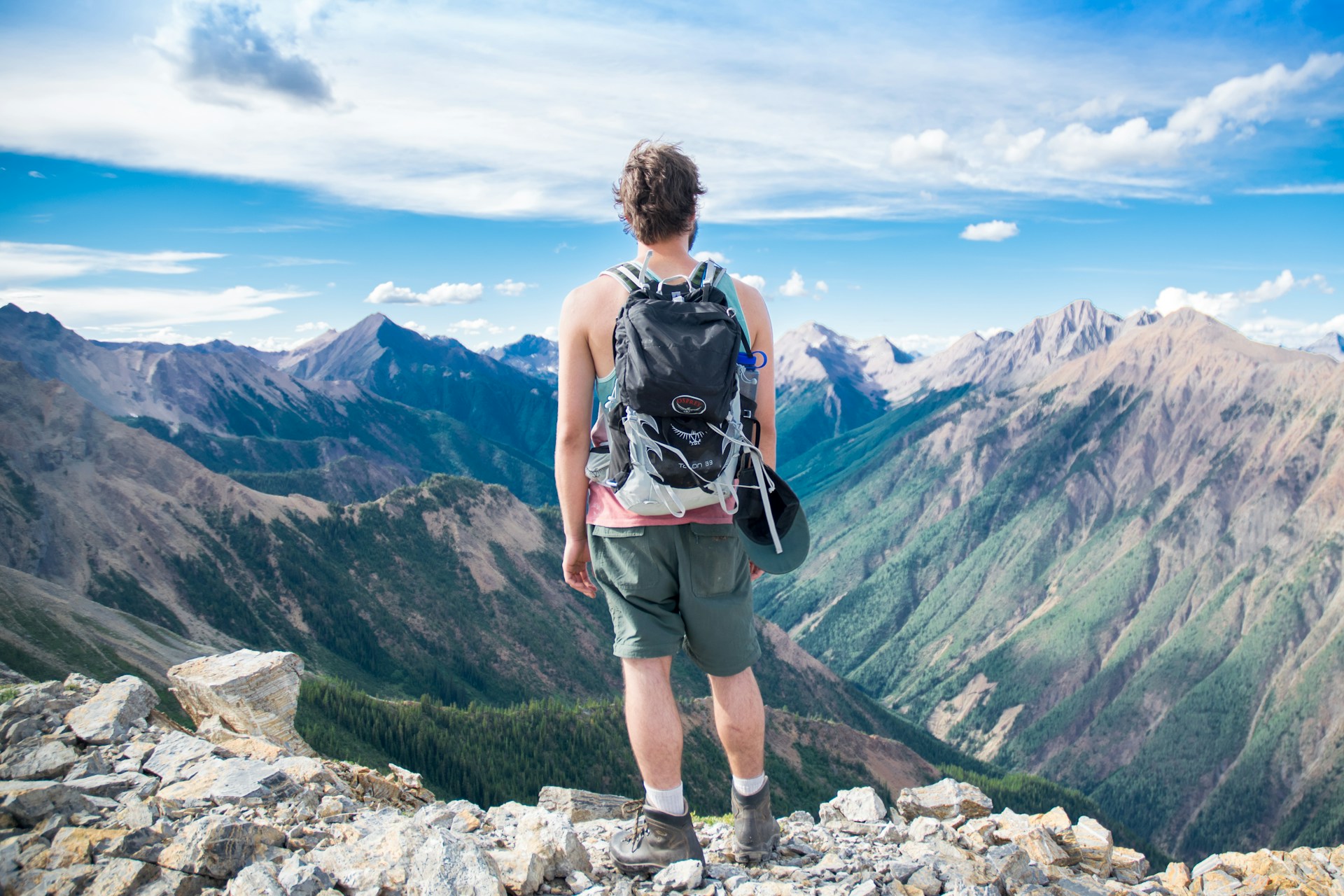 A man looking down into a valley, enjoying the fresh air and taking a pause from a hike.