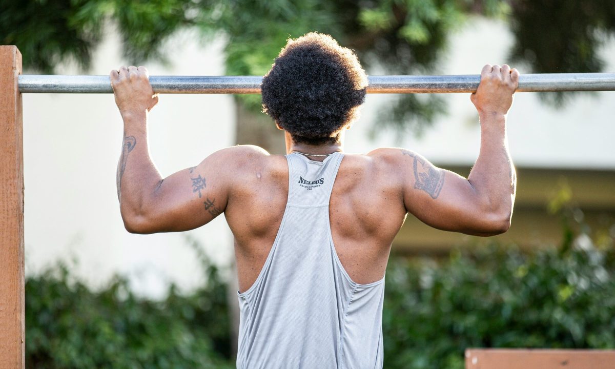 Man wearing white shirt outside doing pull ups exercise on silver bar