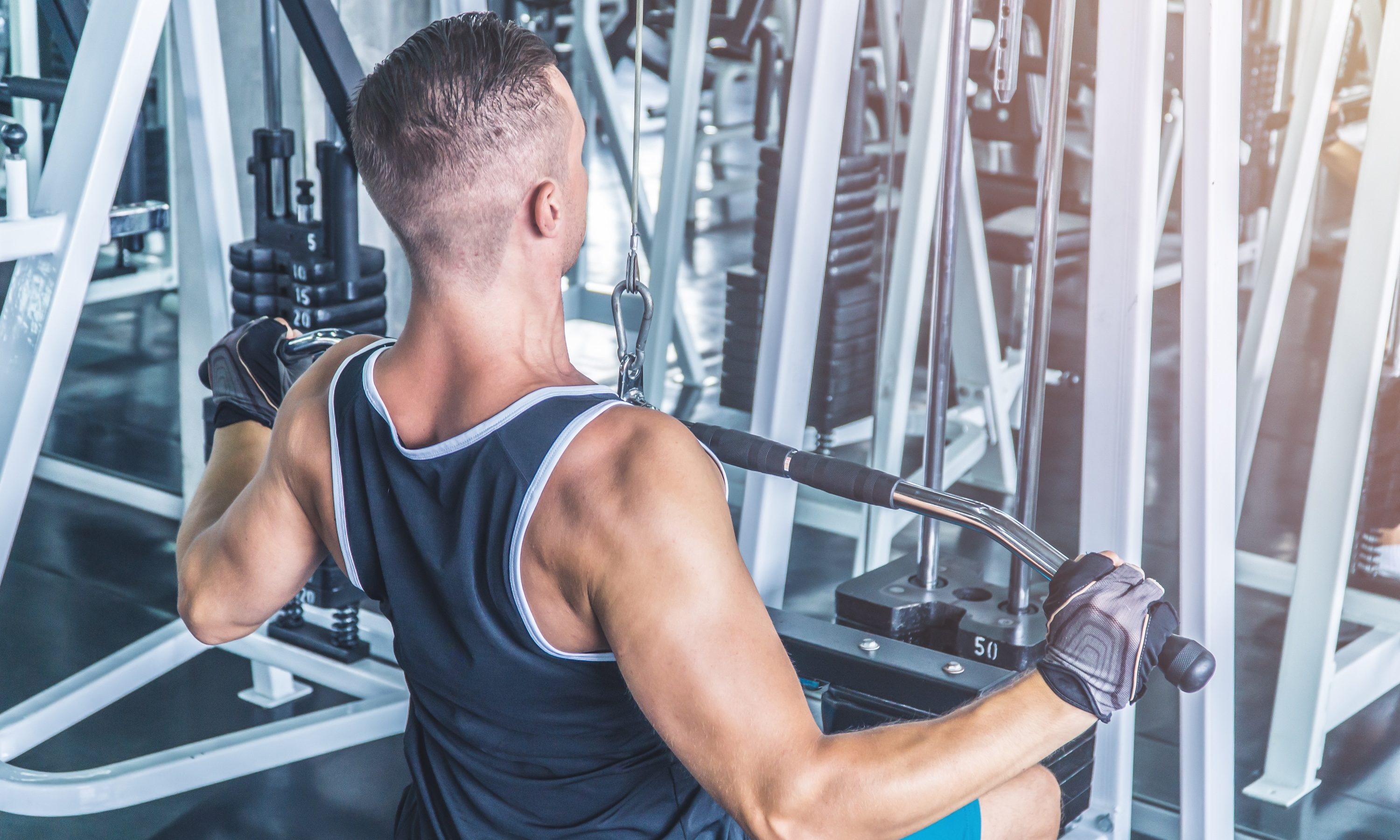 Caucasian muscular man using pull down machine in the gym, weight lifting workout.