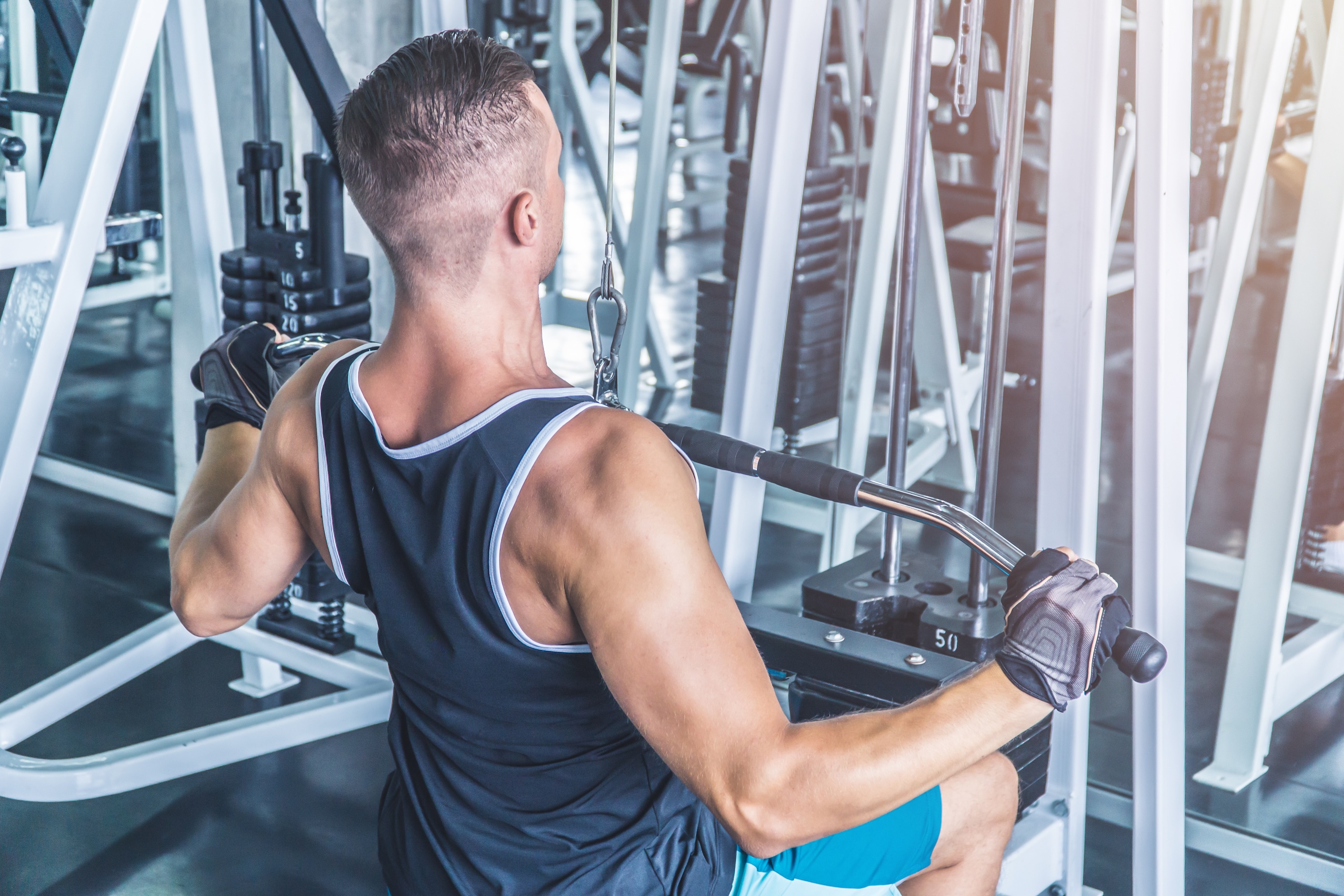 Caucasian muscular man using pull down machine in the gym, weight lifting workout.