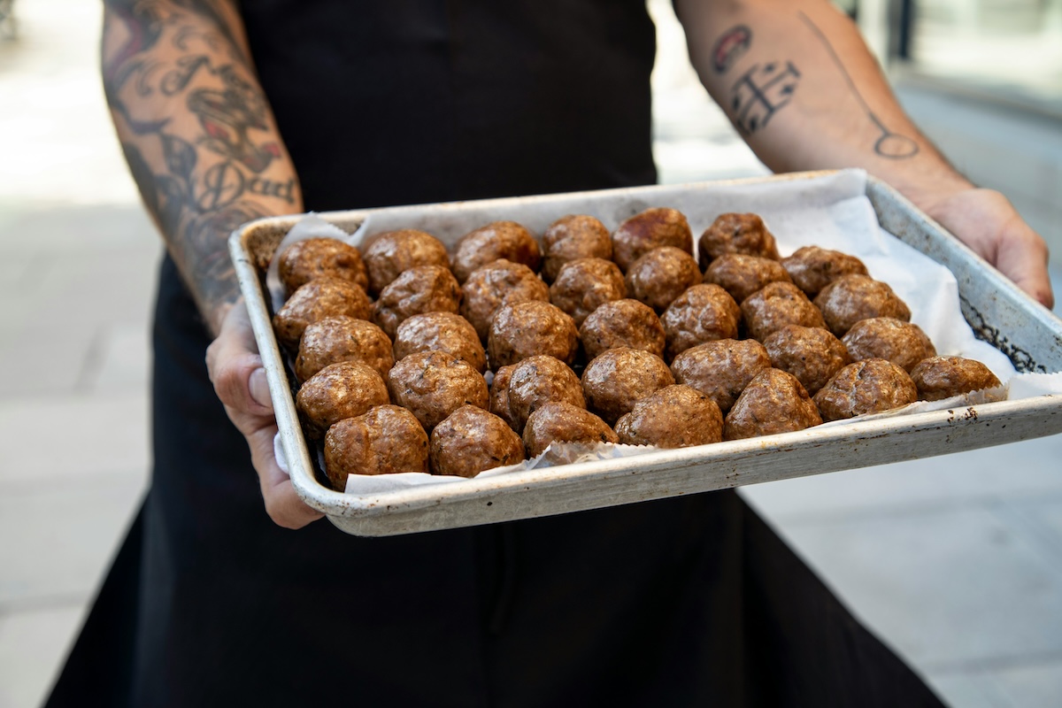 a man with tattoos carrying meatballs on baking sheet