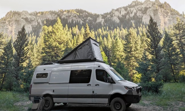 Camper van outfitted with Super Pacific's CloudCap pop-up roof tent parked among a stand of trees.