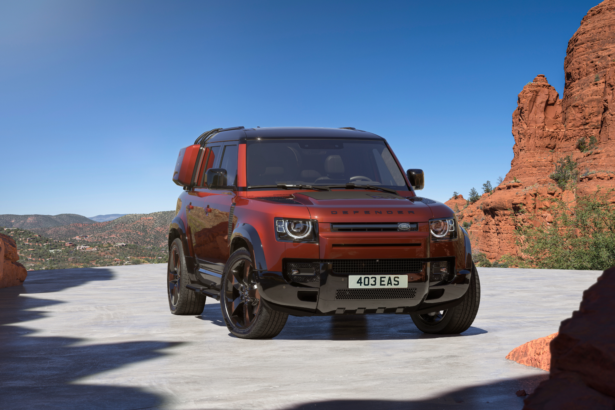 2025 Defender 110 Sedona Edition parked on desert sand with rocky hills in the background right front three-quarter view.