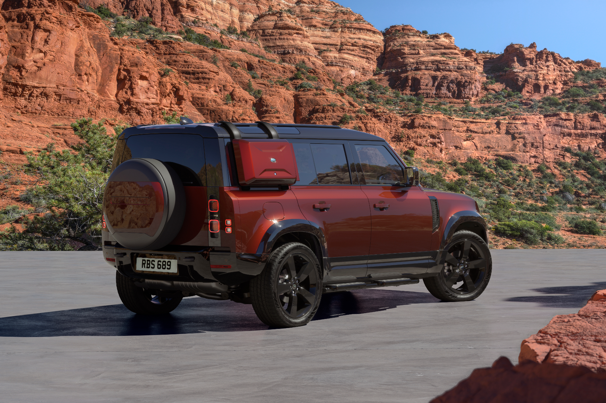 2025 Defender 110 Sedona Edition parked on desert sand with rocky hills in the background right rear three-quarter view