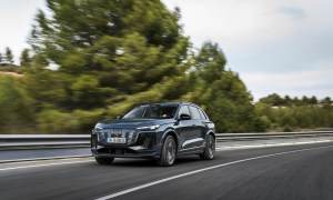 Audi Q6 e-tron driving on a highway with trees, land, and ocean in the background.