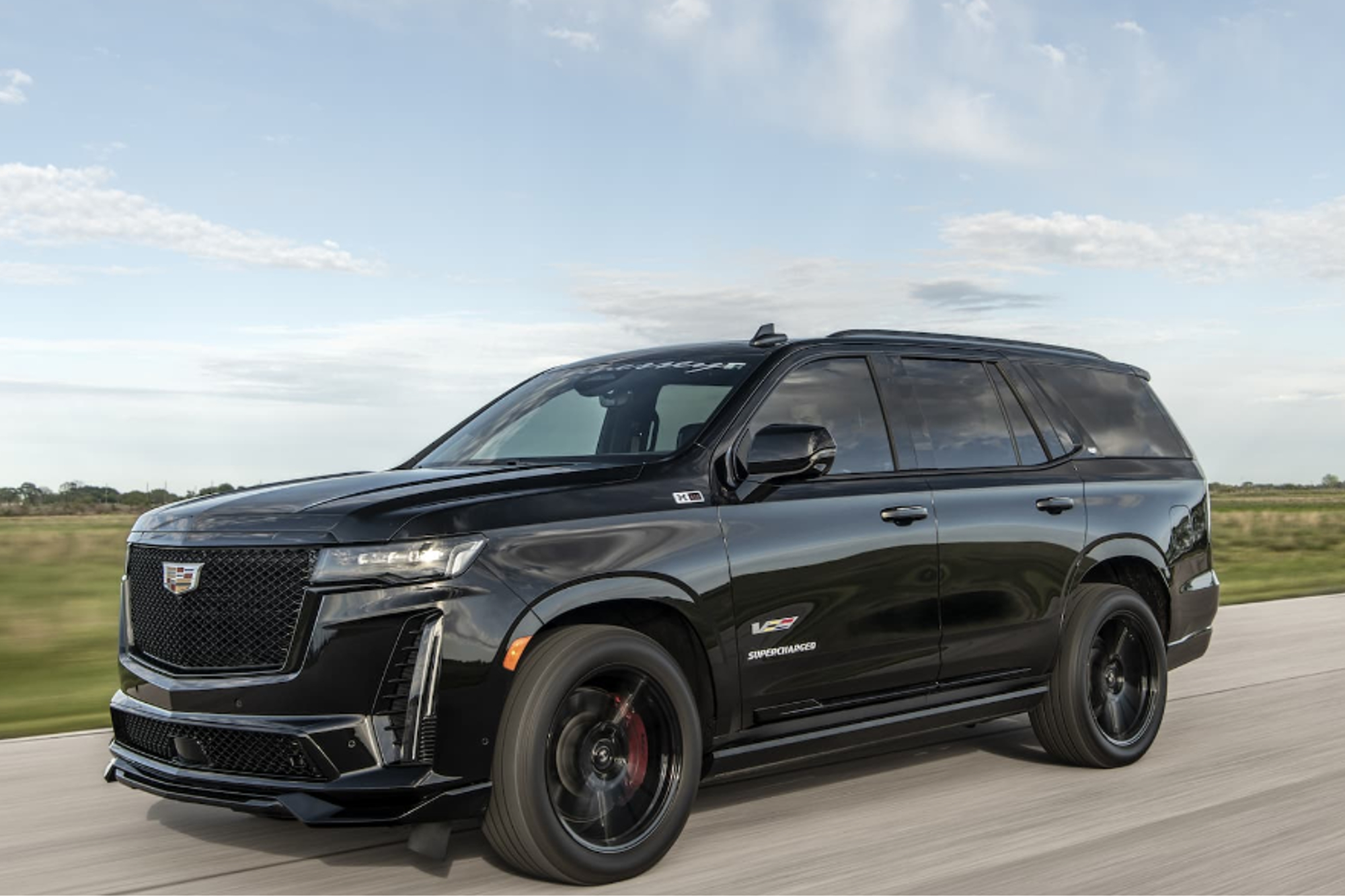 Hennessey H850 Cadillac-V conversion left front three-quarter image driving on a road with grassy field in the background.