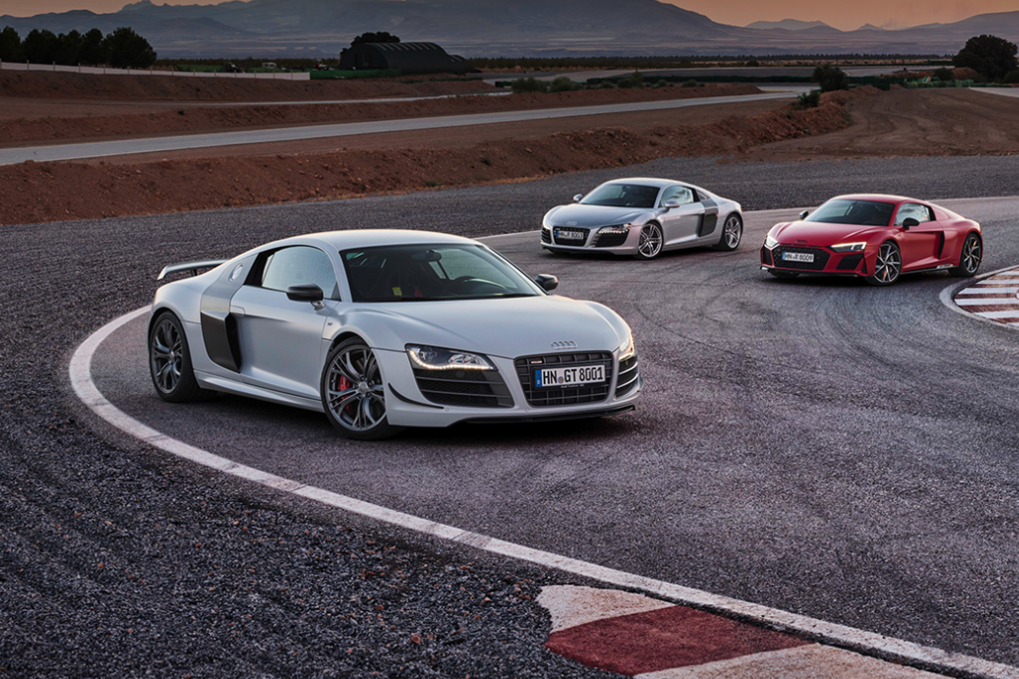 Three Audi R8s on a racetrackwith distant mountains in the background.