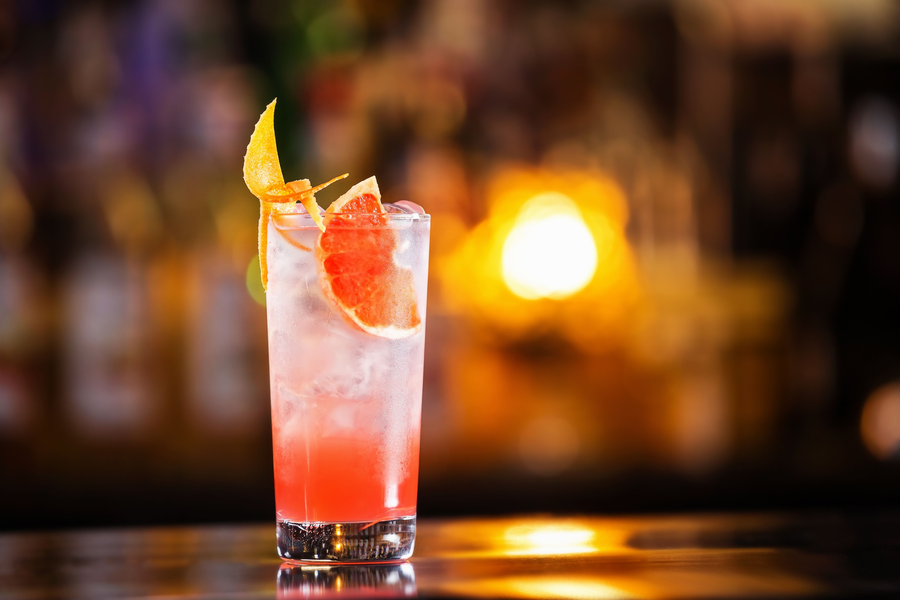 Closeup glass of greyhound cocktail decorated with grapefruit at bright bar counter background.