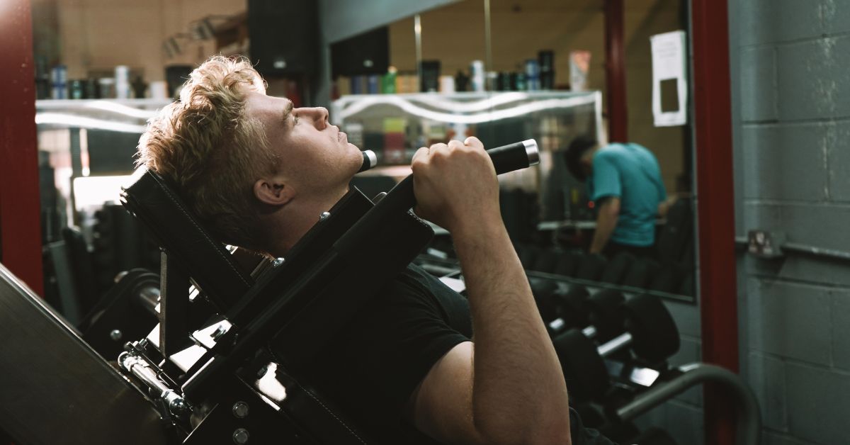 blonde-haired man doing a hack squat on a hack squat machine