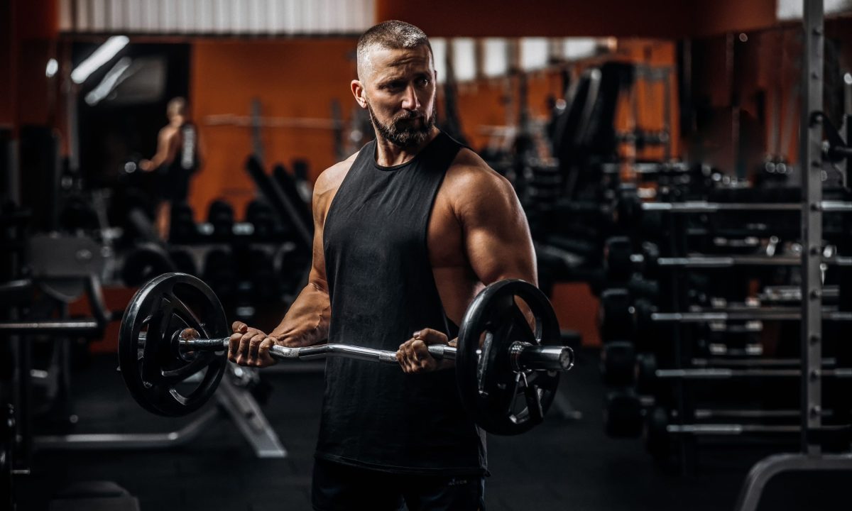 Fit strong man doing biceps curl with barbell in gym