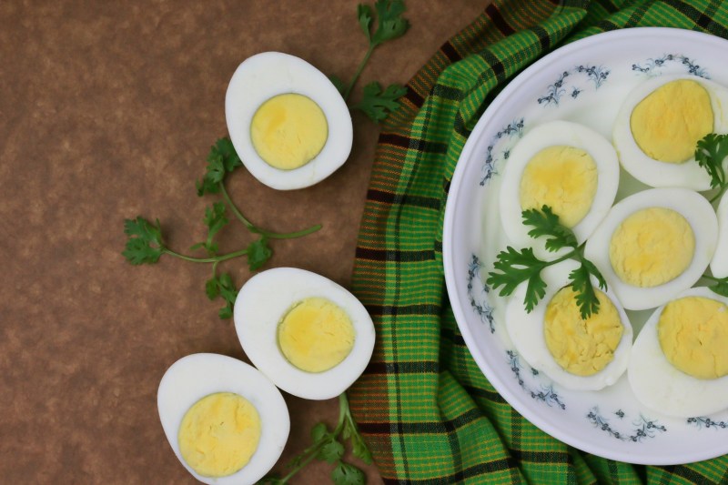 Hard-boiled eggs sliced open in half on brown countertop and white plate with green herbs