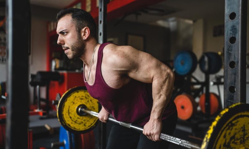 Man doing barbell rows. red vest