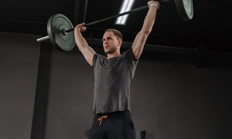 Man in gym doing overhead press or military press with barbell