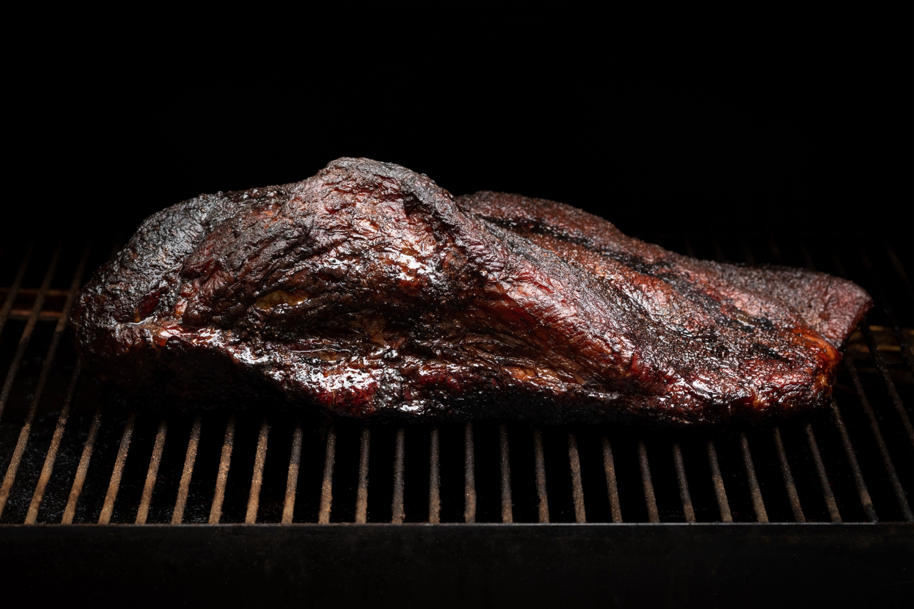 Slow cooked beef brisket on the grill grates of a smoker barbecue, in a cooking background
