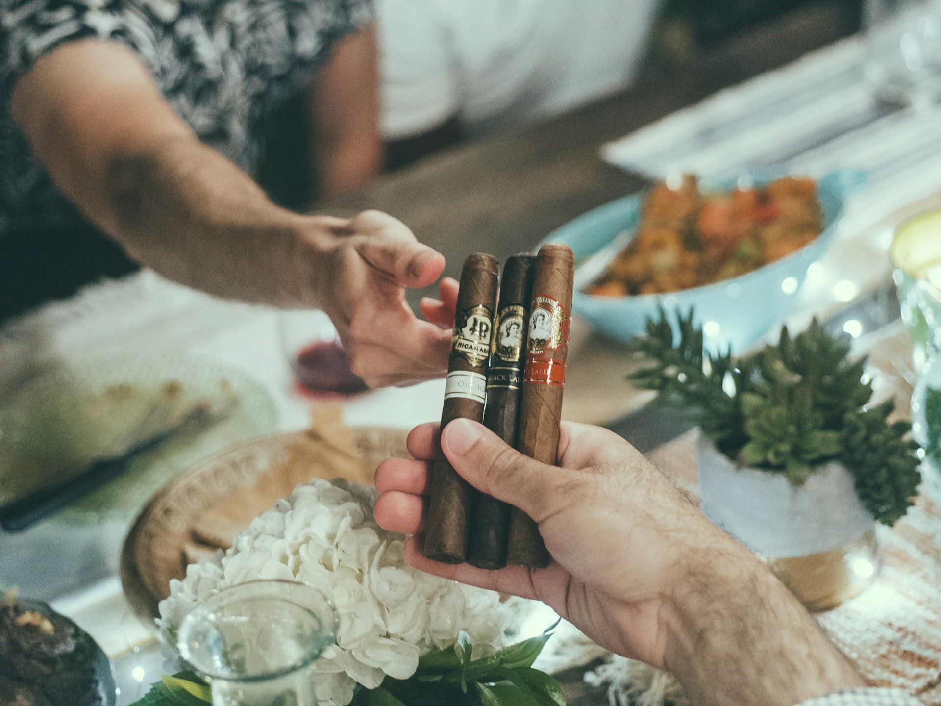 Man passing a few La Palina cigars over a dinner table to a friend.