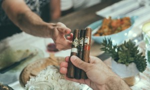 Man passing a few La Palina cigars over a dinner table to a friend.