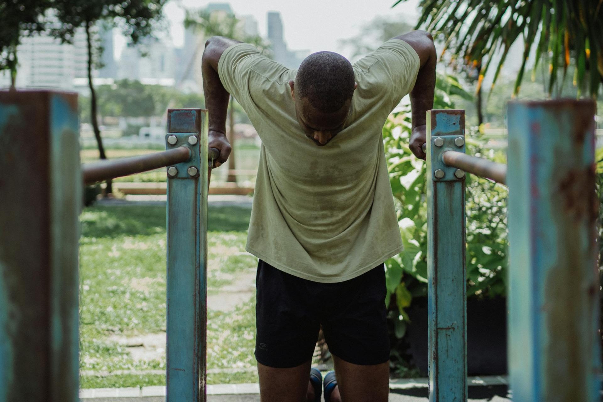 Man wearing a T-shirt and shorts doing dips exercise on metal bars outside