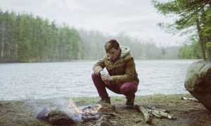 A man sitting next to a campfire near a lake