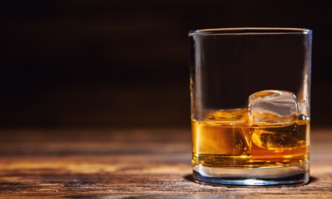 Glass of whiskey with ice cubes served on wooden planks