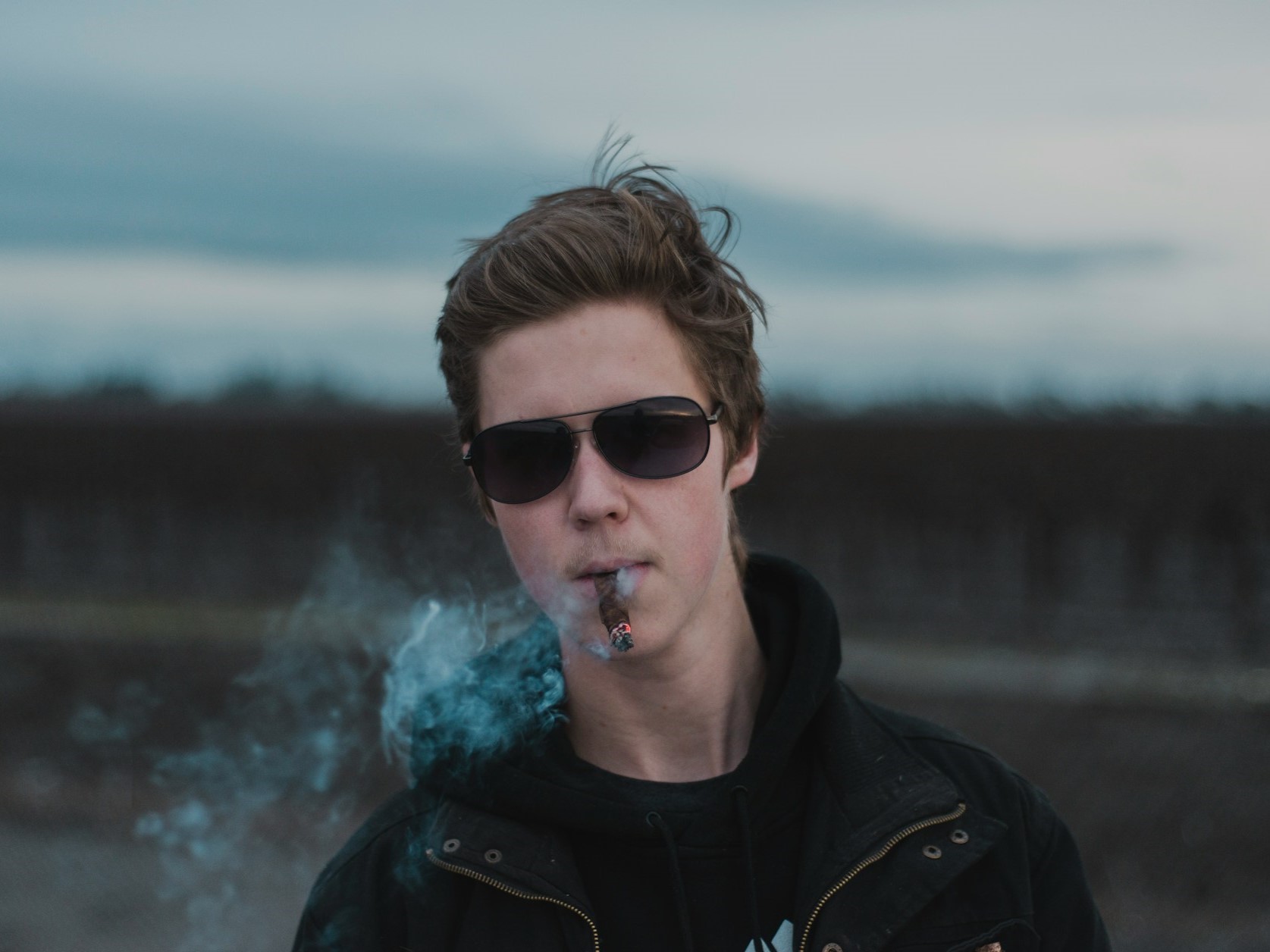 Young man enjoying a cigar outside on a gloomy day.