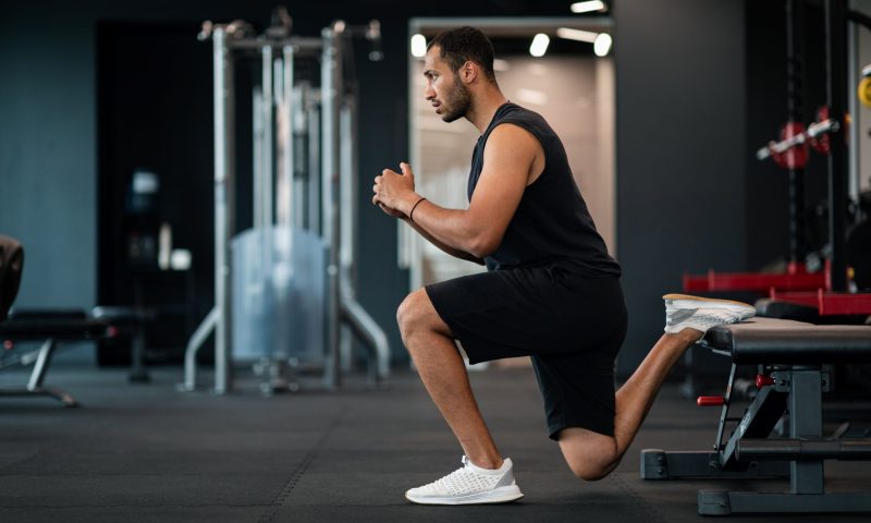 Man in gym with shorts doing Bulgarian split squat exercise in gym