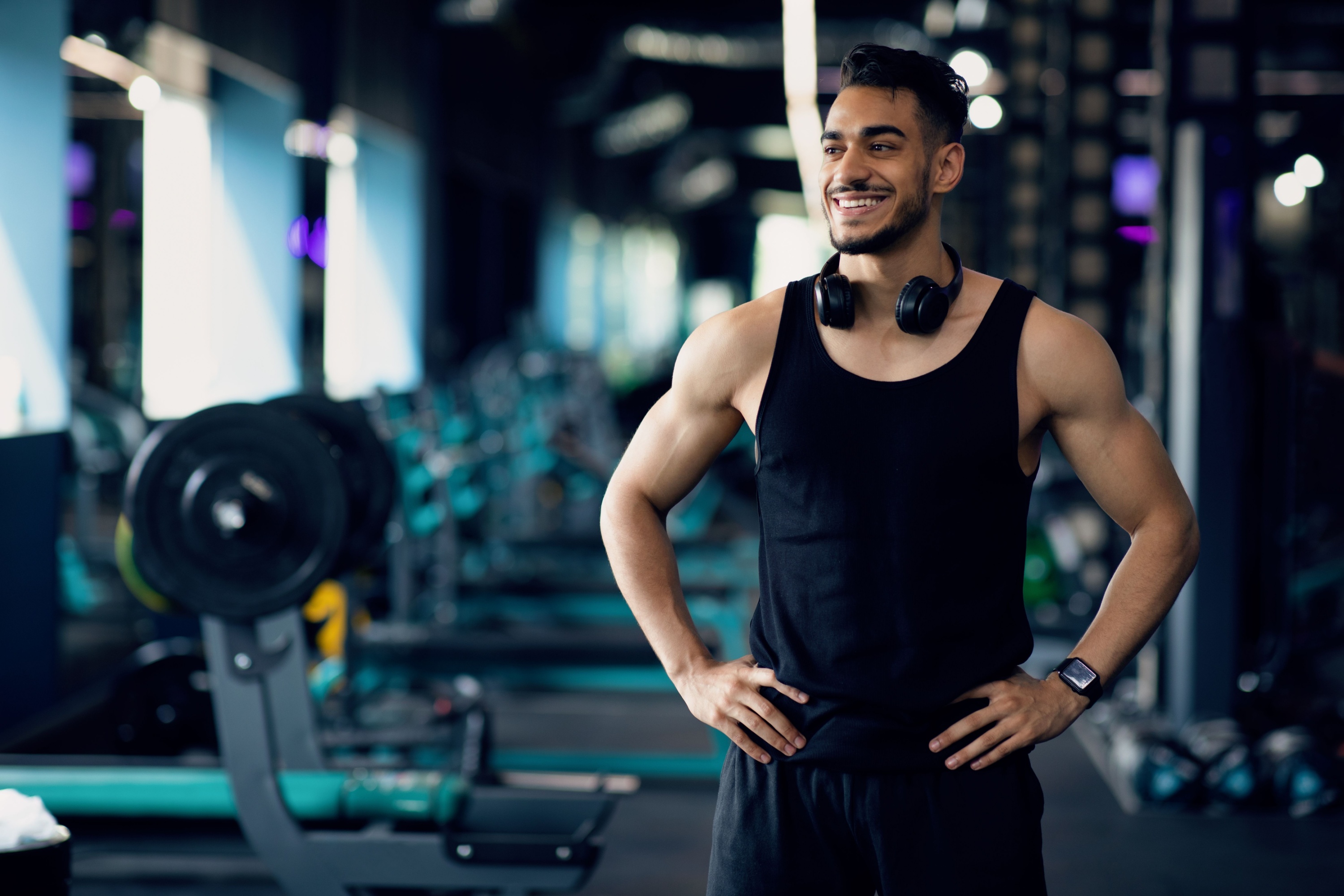 Man in gym wearing a black tank top standing smiling black headphones