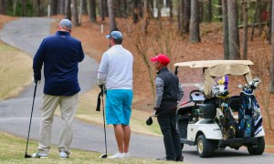 Golfers standing around with a gof cart to the side.
