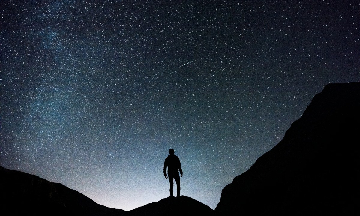 A man standing on a hill while watching a shooting star