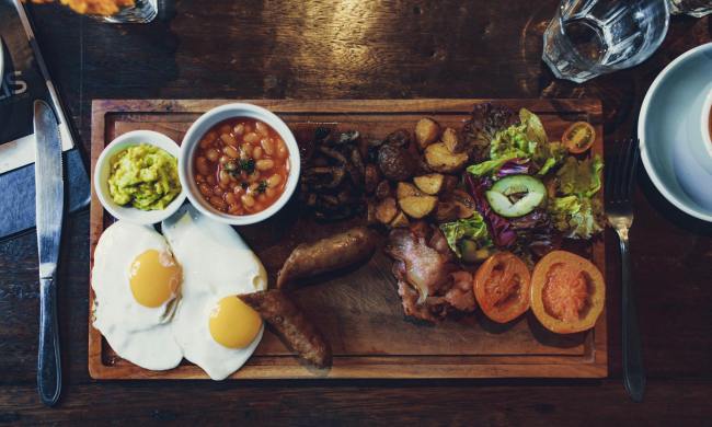 Cutting board with cooked steak, fried eggs, beans, vegetables