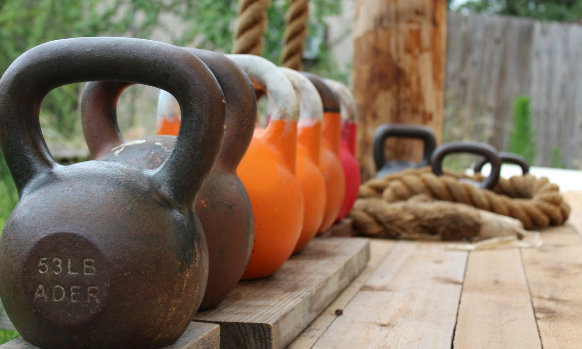 Line of kettlebells on wooden deck outside next to ropes
