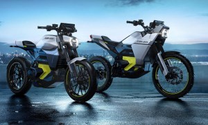 can am origin and pulse electric motorcycles parked on wet pavement with a lighted city river in the background
