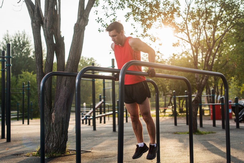 Man working out doing chest dips on parallel bars outside
