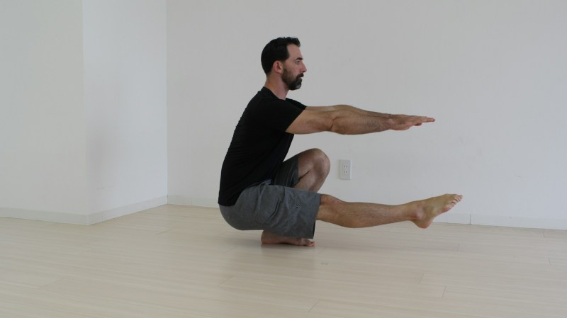 Man in a black T-shirt doing pistol squat inside on wooden floor