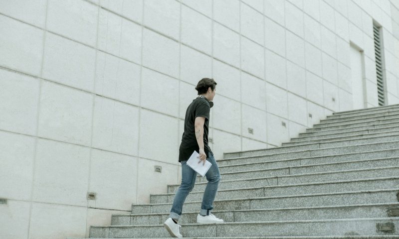Man walking up stairs wearing jeans and white sneakers outside concrete