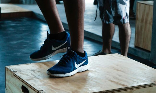 Close-up man legs wearing blue sneakers doing step-up exercise in gym