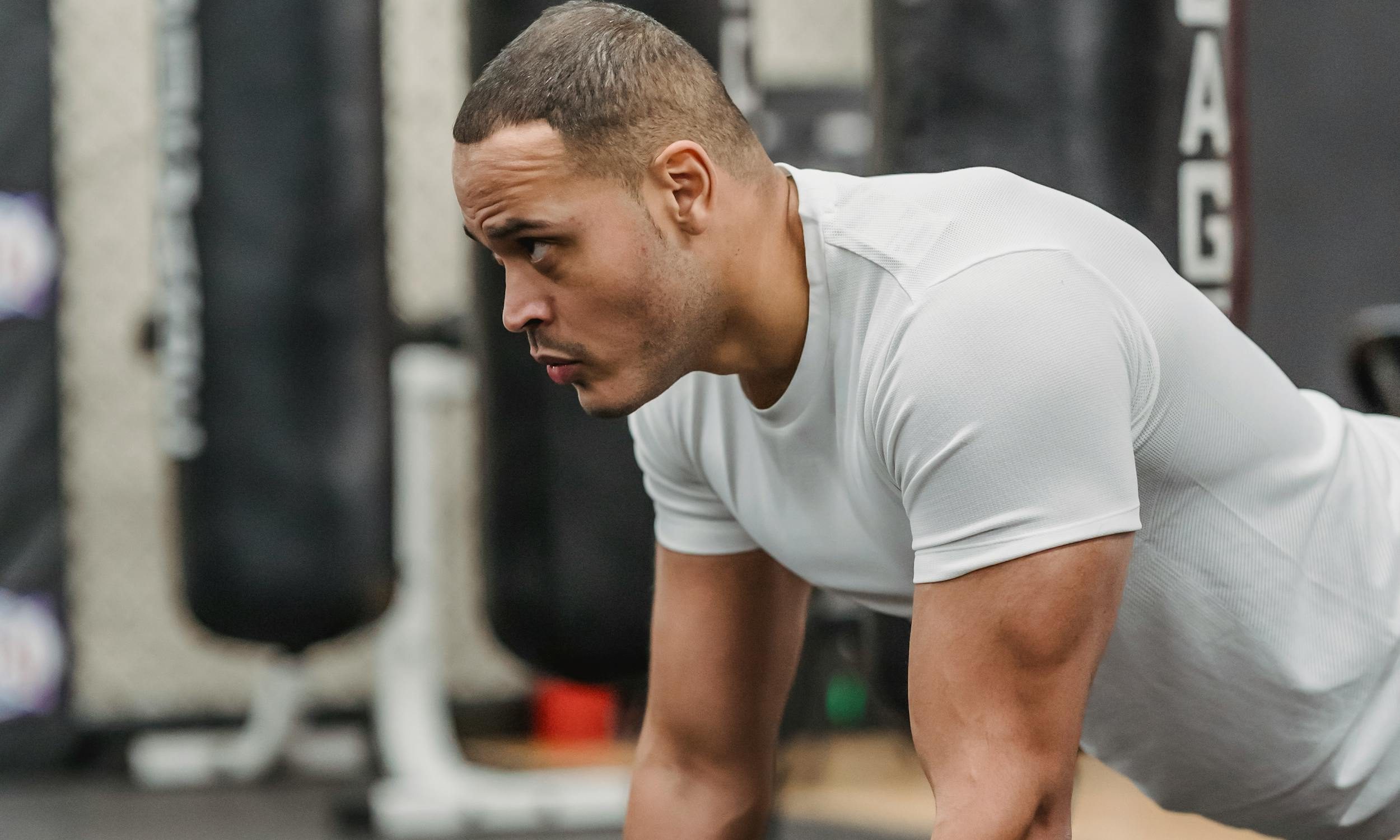 side view of man white shirt doing renegade dumbbell row