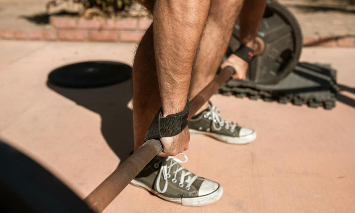 close up of mans hands picking up barbell bent-over barbell row on floor outside
