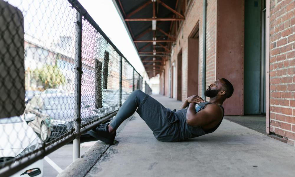 Man doing situps using a fence for help outside on a concrete floor