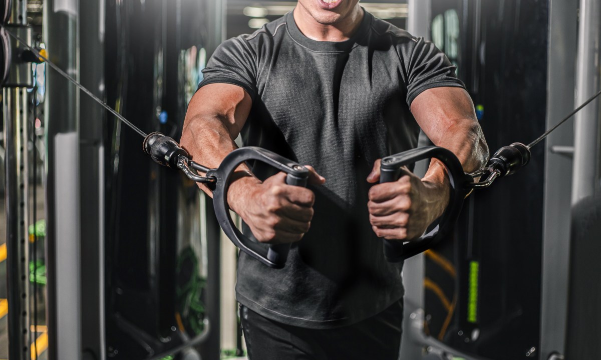 Man doing standing cable chest press exercise in gym on cable machine