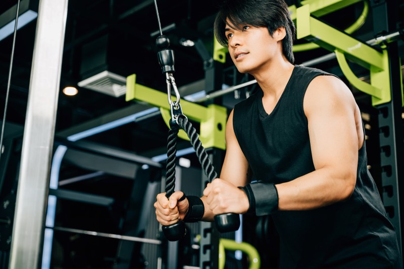Man in gym with a black tank top doing cable pullover exercise with cable machine rope pulley
