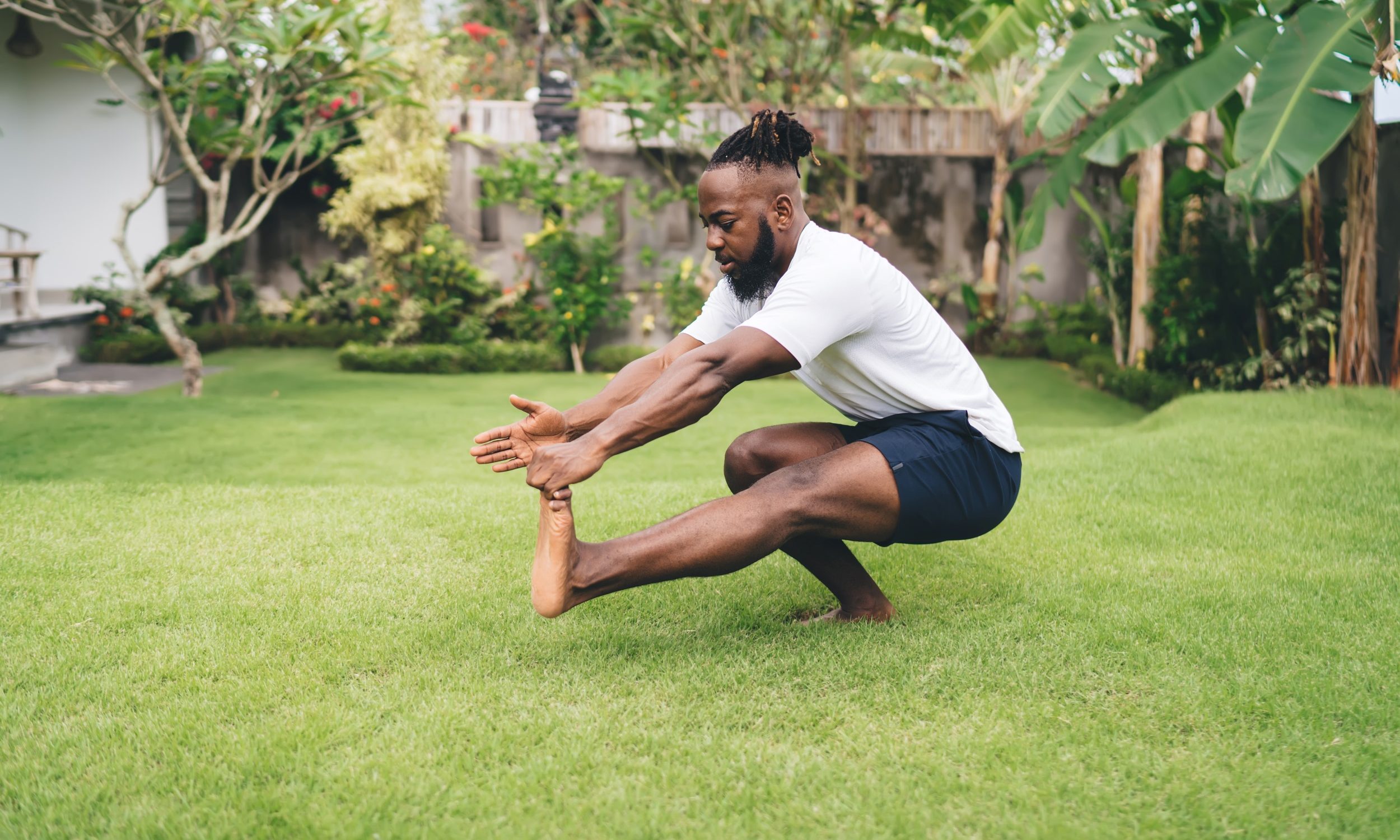 Man wearing white T-shirt and black shorts doing pistol single-leg squat soutside