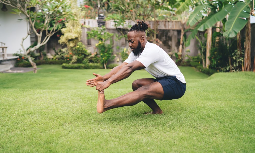 Man wearing white T-shirt and black shorts doing pistol squat single-leg squat outside on grass