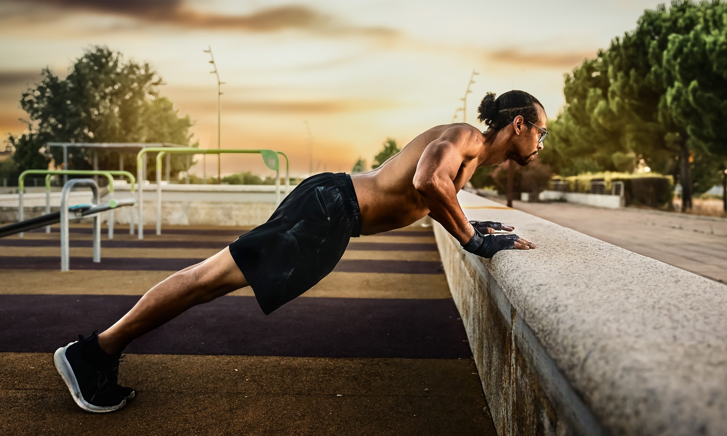 shirtless man outside sunset doing incline pushup on wall.