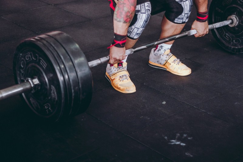 Man bending down to pick up barbell for bent-over barbell row close up of feet and hands and barbell